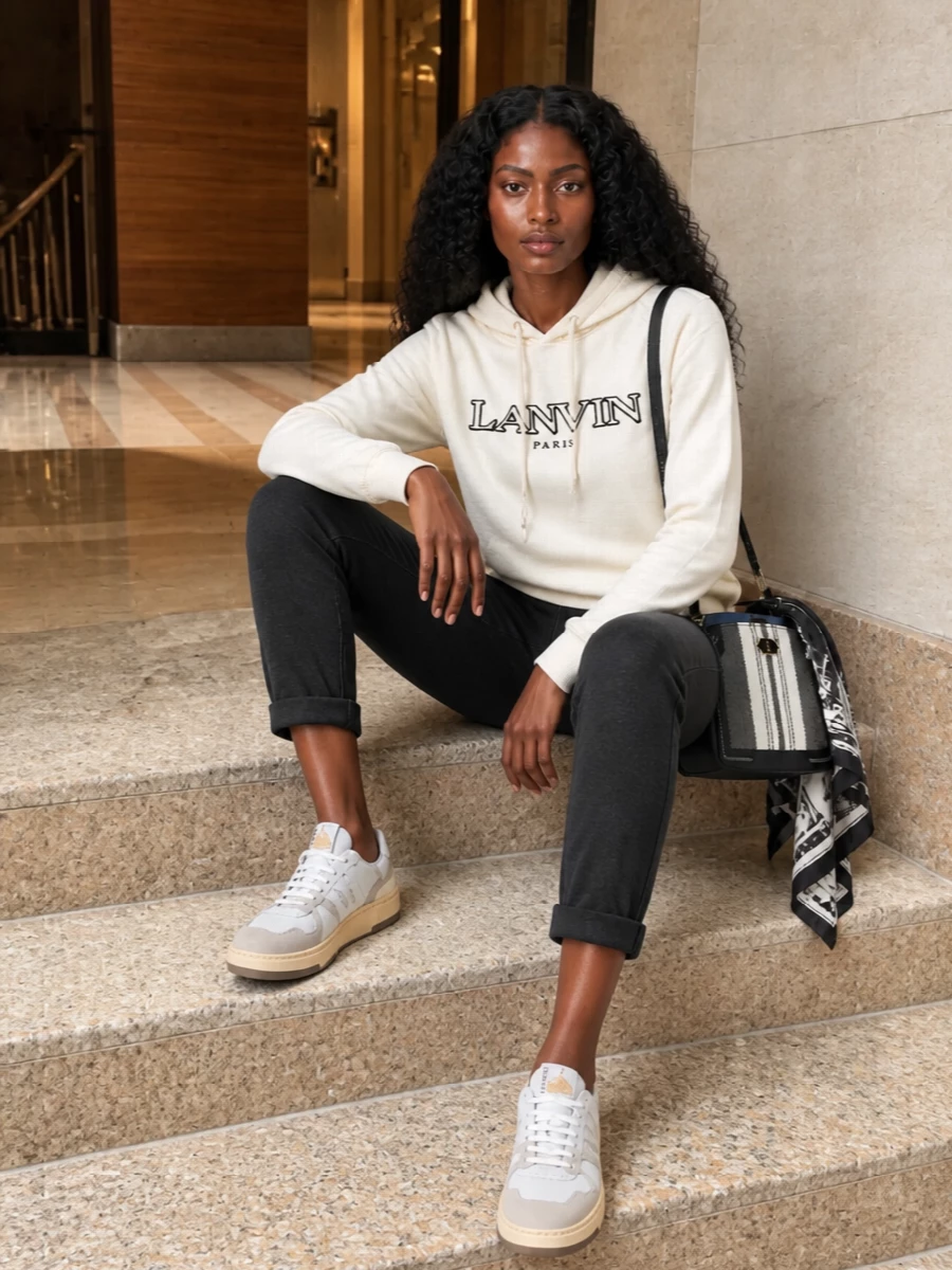 An ivory logo hoodie pairs with slim, charcoal knit joggers for a relaxed but intentional base in graphic neutrals. Paneled sneakers keep the energy sporty, while the structured striped bag and printed scarf add a precise, Paris-born finish. It is an easy city uniform that reads casual yet considered from coffee runs to low-key dinners.