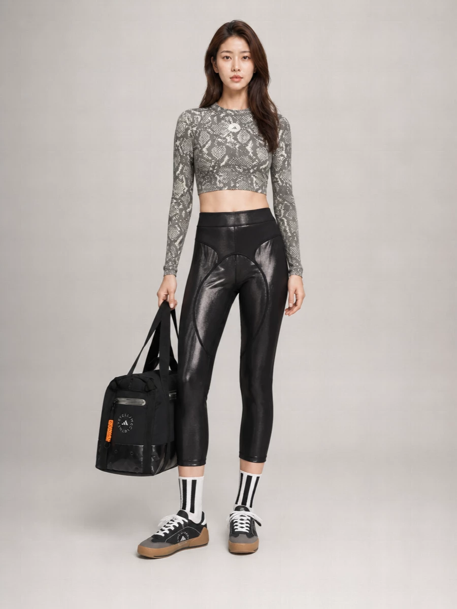 A sculpted, studio-ready set that leans into monochrome animal textures and metallic shine for a sharp Y2K-sport mood. The cropped snakeskin top locks to the high-rise leggings, while sleek black trainers and striped socks keep the energy grounded and agile. A technical oversized tote finishes it with a practical, city-commute attitude that still feels club-adjacent after dark.