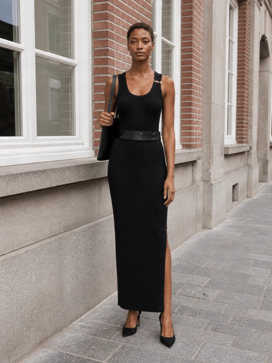 A long, uninterrupted black column anchored by a suede stiletto and a flat, structured shoulder pouch keeps the mood impeccably quiet and assured. The Margiela belt adds just enough architecture at the waist, letting the dress’s gold hardware be the only bright note. It is a pure, evening-ready take on minimalist sensuality that moves easily from dinner reservation to late cocktail bar.