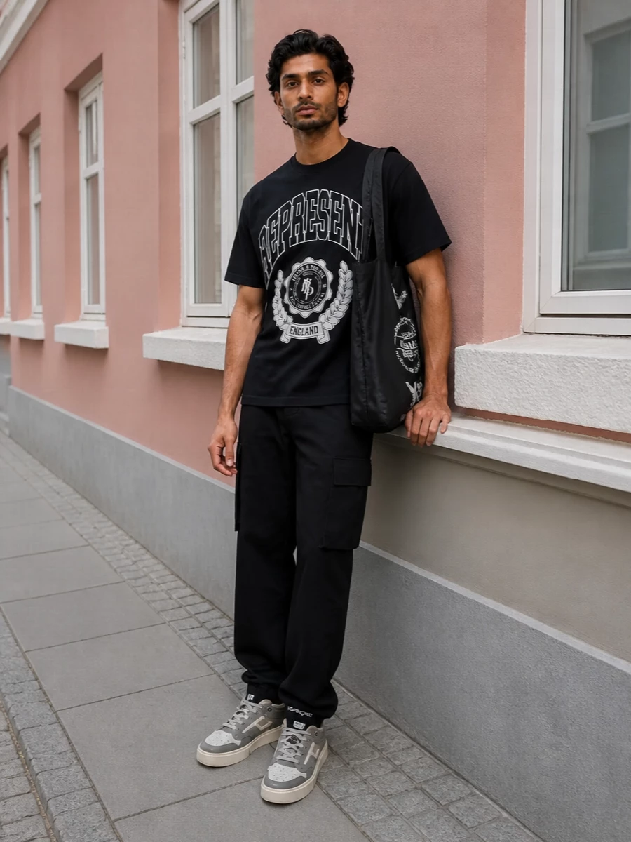 This is a tight monochrome streetwear outfit built around that varsity Represent tee, grounded with black cargos that keep the silhouette straight and easy. Chunky taupe court sneakers and a slouchy Y-3 tote soften the head-to-toe black just enough, while the subtle logo socks finish it with a low-key, considered edge.