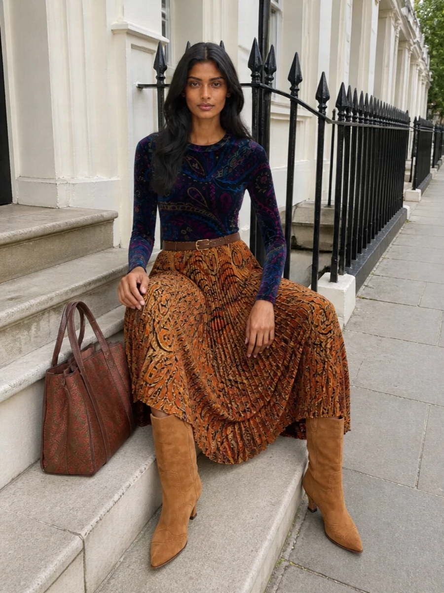 Rich autumn tones wrap around the body, with the paisley pleated skirt anchored by a slim jewel toned velvet top that keeps the story bohemian but refined. Camel suede boots and a structured paisley tote keep the palette warm and grounded, while a slim burgundy belt quietly sharpens the waistline. It is an easy day‑into‑evening pairing that feels romantic, collected and seasonally right without ever feeling overdone.
