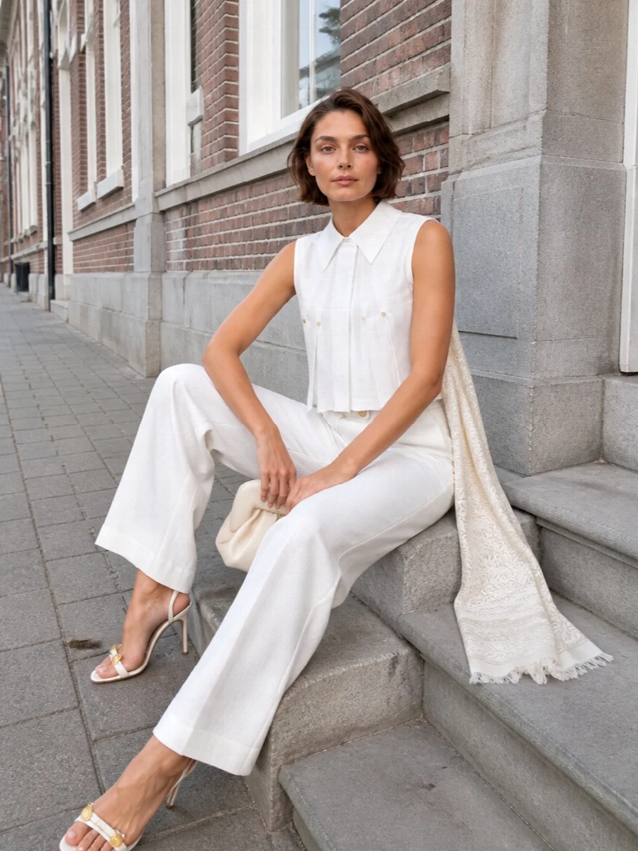 An all-Elisabetta Franchi white and gold story, this pairing of sculpted sleeveless blouse and high-waisted wide-leg trouser reads like modern city suiting for warm nights. The crisp pleats and clean column line keep the silhouette sharp yet airy, while white stiletto sandals and a buttercream clutch refine the palette without breaking the quiet luxury mood. A tonal paisley stole adds just enough softness for terraces, yachts and late dinners under warm light.