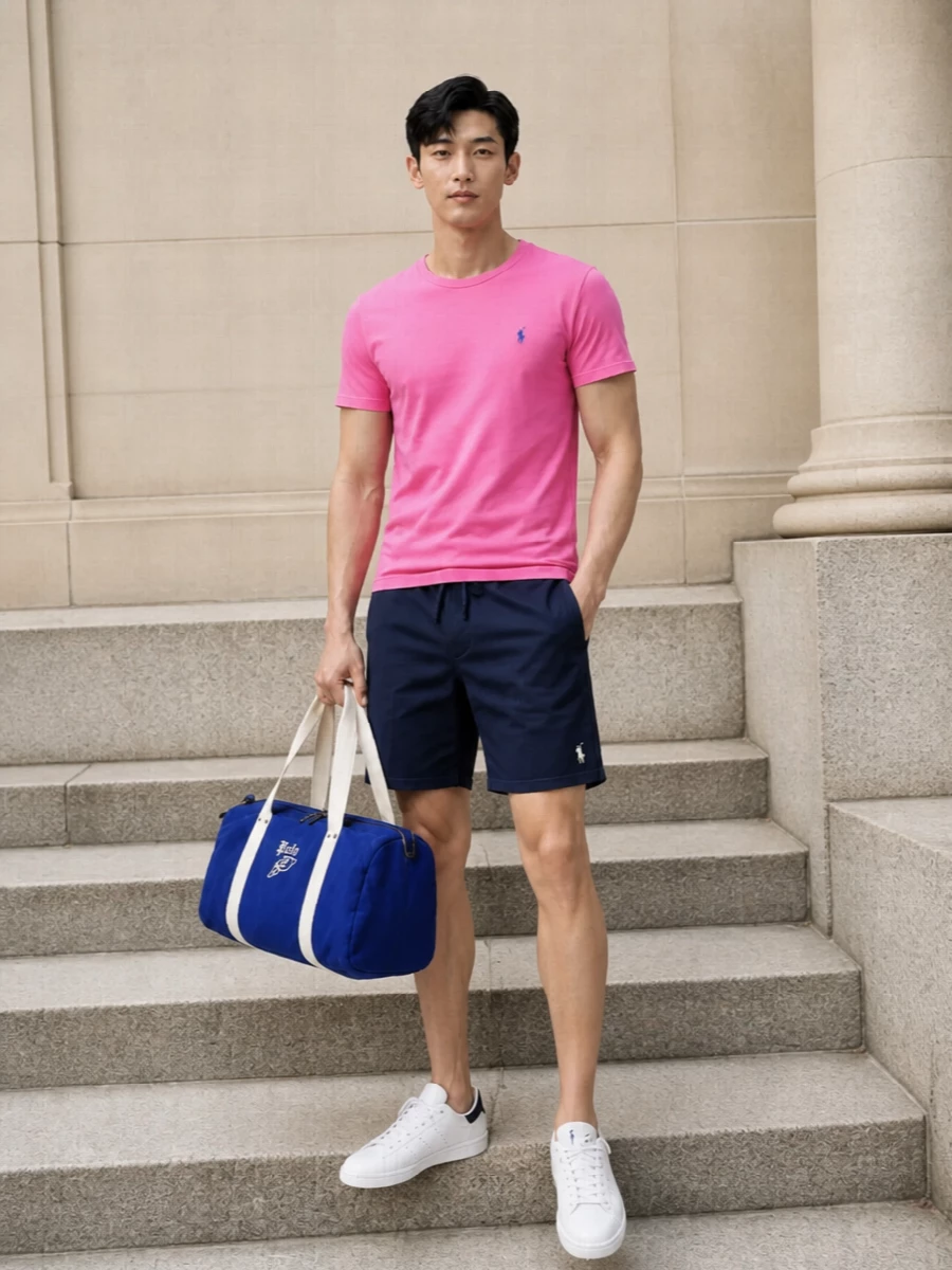 Bright pink meets deep navy for a clean, collegiate take on casual summer dressing. The tee stays the hero, with unfussy deck shorts and crisp white sneakers keeping the silhouette relaxed and sharp. A royal-blue duffle underlines the off-duty, sport-influenced mood without competing with the colour punch up top.