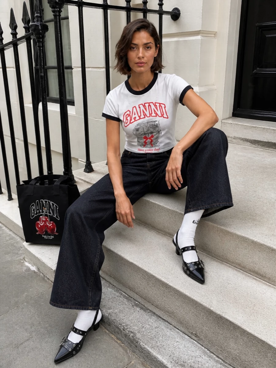 Graphic Ganni energy dialed up but still wearable: the kitten ringer tee meets deep-indigo wide-leg denim for a clean, slightly nostalgic silhouette. Black hardware-slingbacks and a collegiate-style cherry tote pick up the tee’s trims and lettering, keeping everything sharp, playful and city-ready. Off-white logo socks are a tiny nod to sport that softens the heel without losing attitude.