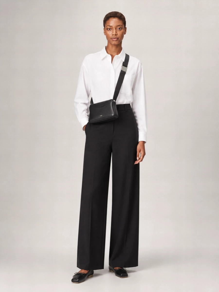 A crisp white shirt and high-waisted black wide-leg trouser create a precise, minimal base that lets the structured Max Mara cross-body quietly lead. The square-toe black flat repeats the bag’s graphic line, so the whole outfit reads as one considered, city-ready uniform. Choosing tailoring over a dress keeps this firmly in the smart day-to-dinner space the bag was designed to live in.