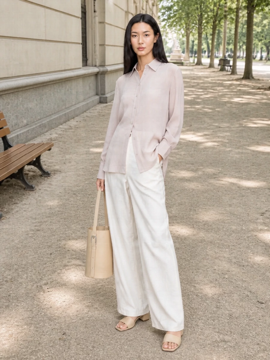 Soft neutrals keep this wide-leg trouser grounded in a calm, modern palette. The sheer taupe shirt floats over the waistband, while cream mules and a structured buttercream bucket bag sharpen the relaxed proportions. An ivory scarf finishes everything with a light, textural whisper rather than a hard accessory line.
