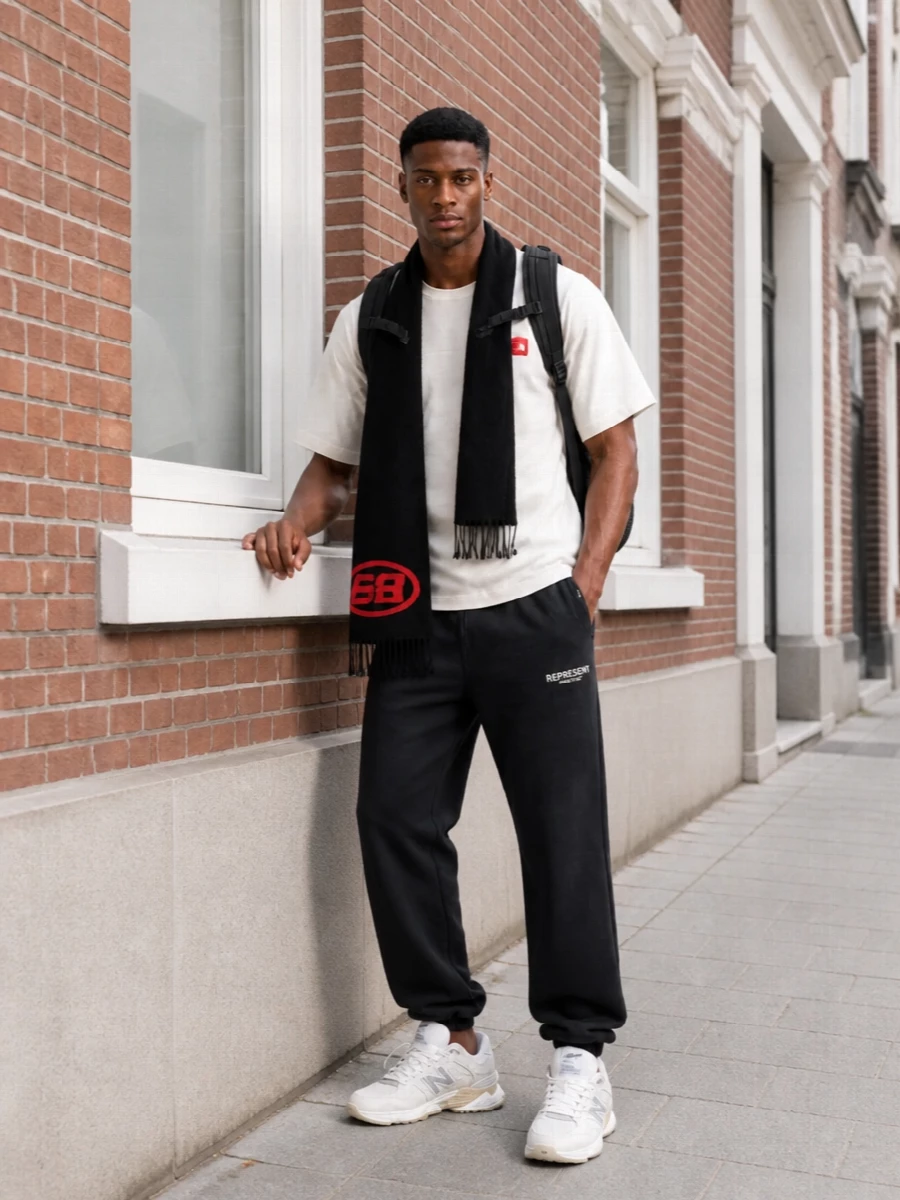 An off white logo tee sits over washed black joggers for a clean, relaxed street-sport base. Off white and beige runners keep the palette soft while the black technical backpack and black‑red scarf sharpen the outdoor energy without feeling loud. The result is an easy commuter uniform that feels considered but still low key for cooler months.