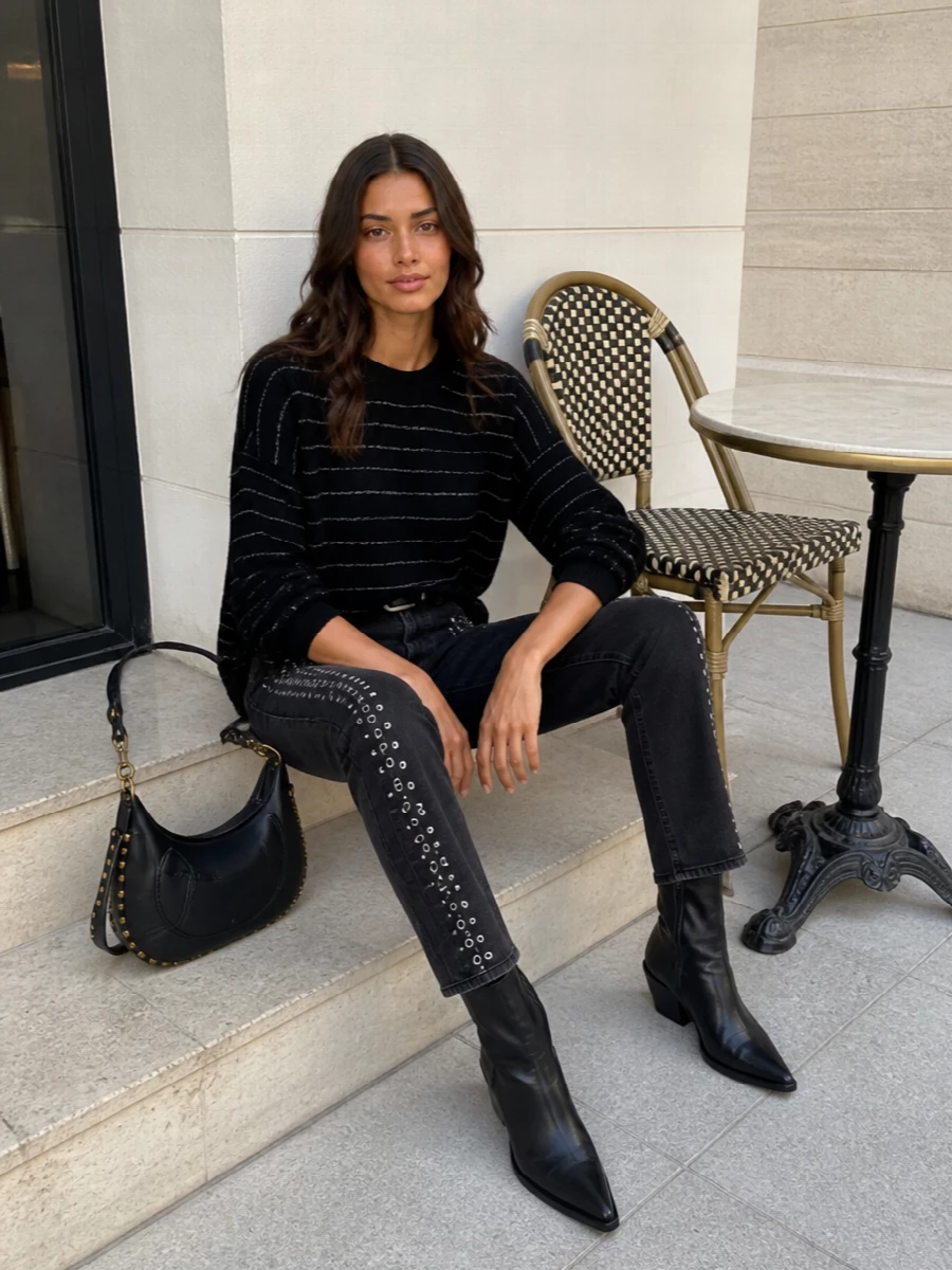 Washed black studded denim meets a softly boxy striped knit, keeping the mood rock-inflected but relaxed. Ankle western boots and a compact studded hobo keep the line clean and leggy, while a simple belt sharpens the high rise so the jeans stay the focus.