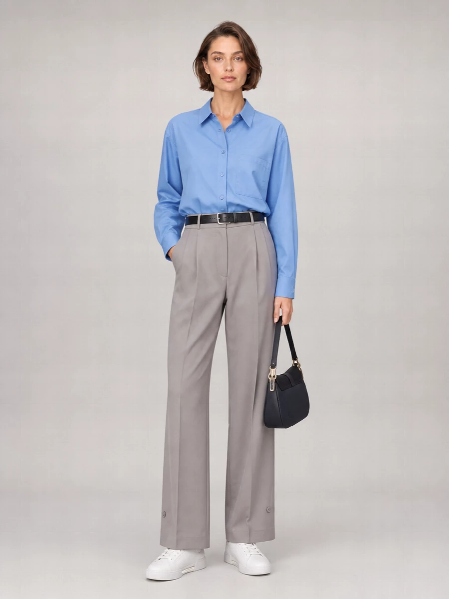 A cornflower blue shirt is tucked into fluid taupe-grey wide-leg trousers for a long, clean line that reads relaxed but intentional. White sneakers keep it grounded and easy, while a navy shoulder bag and slim black belt add just enough structure for desk-to-weekend dressing.