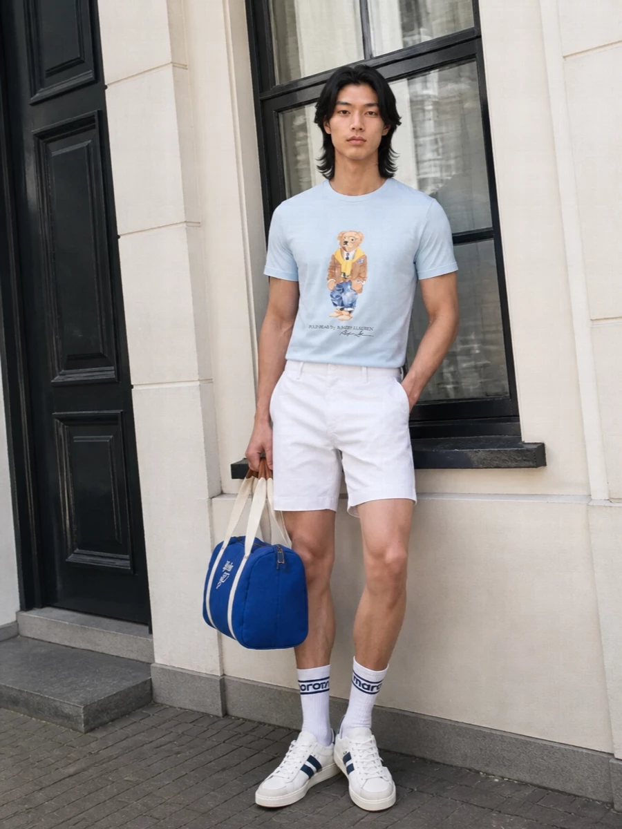 Pale blue, optic white and navy sit in an easy East Coast palette that keeps the Polo Bear tee feeling relaxed but still considered. The tailored chino short and clean court sneakers lift it just enough for city days or smart-casual weekends, while the collegiate bag and socks keep the mood playful rather than precious.