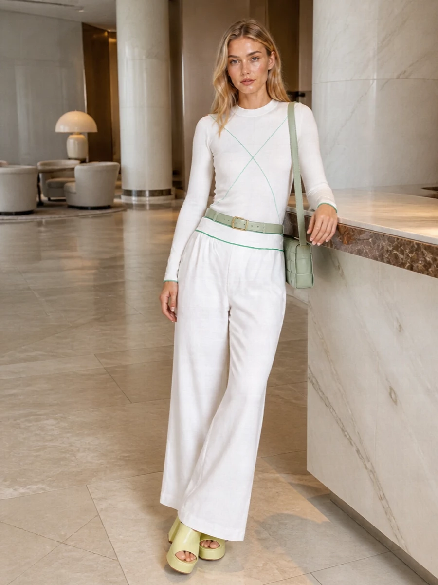 Soft white and clean lines set a calm base, with precise hits of green stitching and accessories giving the outfit its quiet tension. The high waist and platform height keep the wide leg elongated and sharp, while a compact woven bag and slim belt pull the palette together with subtle polish.