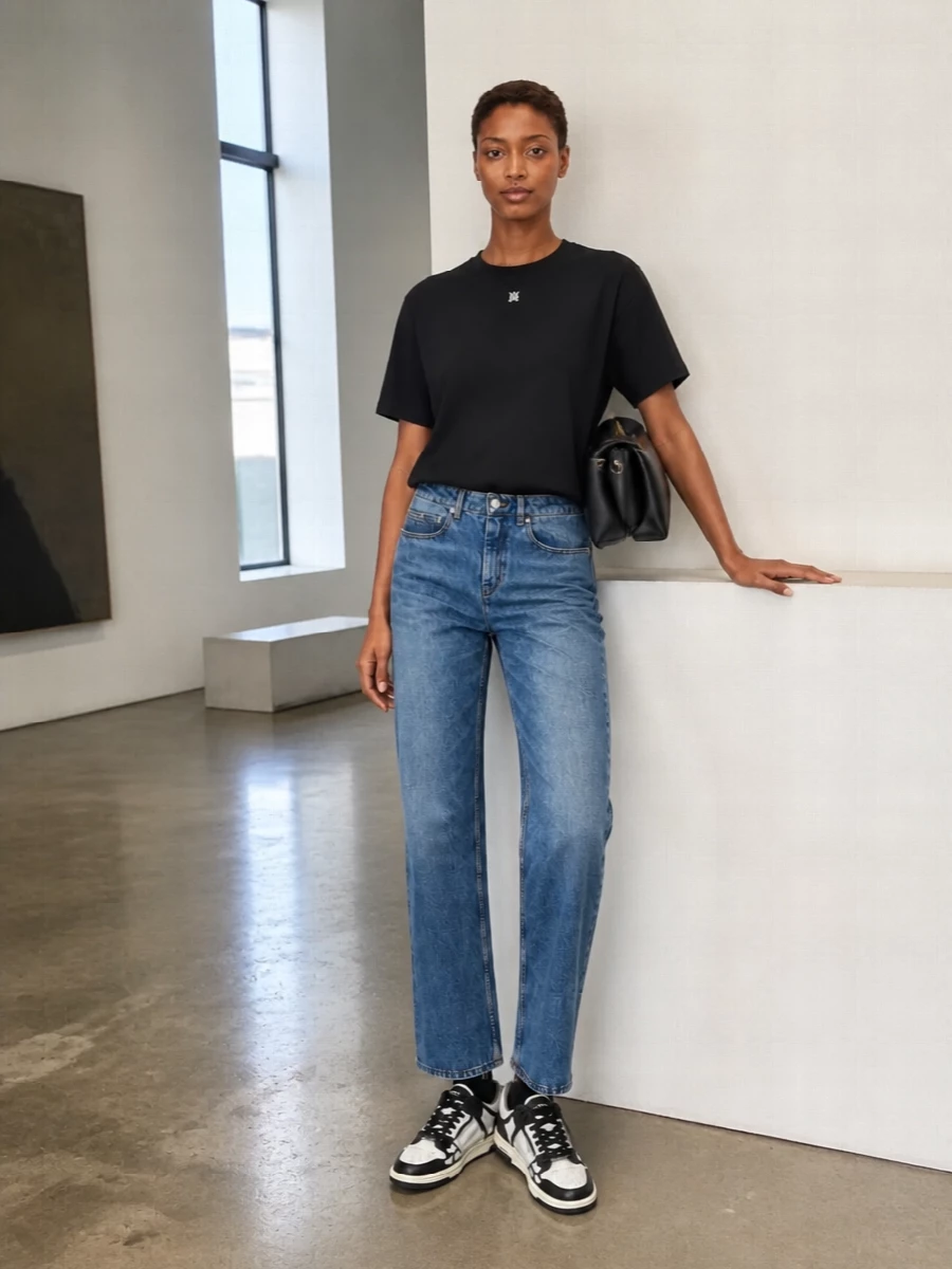 A black Amiri tee and straight faded denim give an easy, graphic base that reads clean rather than casual. Monochrome Amiri sneakers keep the line modern and streamlined, while a structured black shoulder bag sharpens everything just enough for city days and low-key nights. The result is quietly branded streetwear with a calm, polished finish.