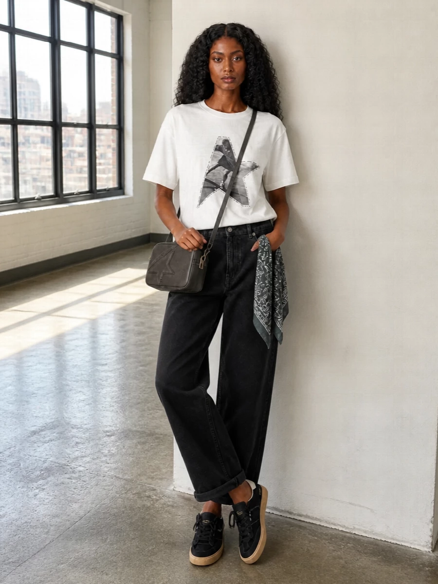 A boxy graphic tee meets washed black wide-leg denim for a clean, downtown take on sport-inflected streetwear. Black suede sneakers and a compact star camera bag keep the palette tight and intentional, while a charcoal bandana adds a subtle nod to classic skate and bandana culture. The result feels relaxed but sharply edited, ideal for city days that move from coffee runs to late-night walks.