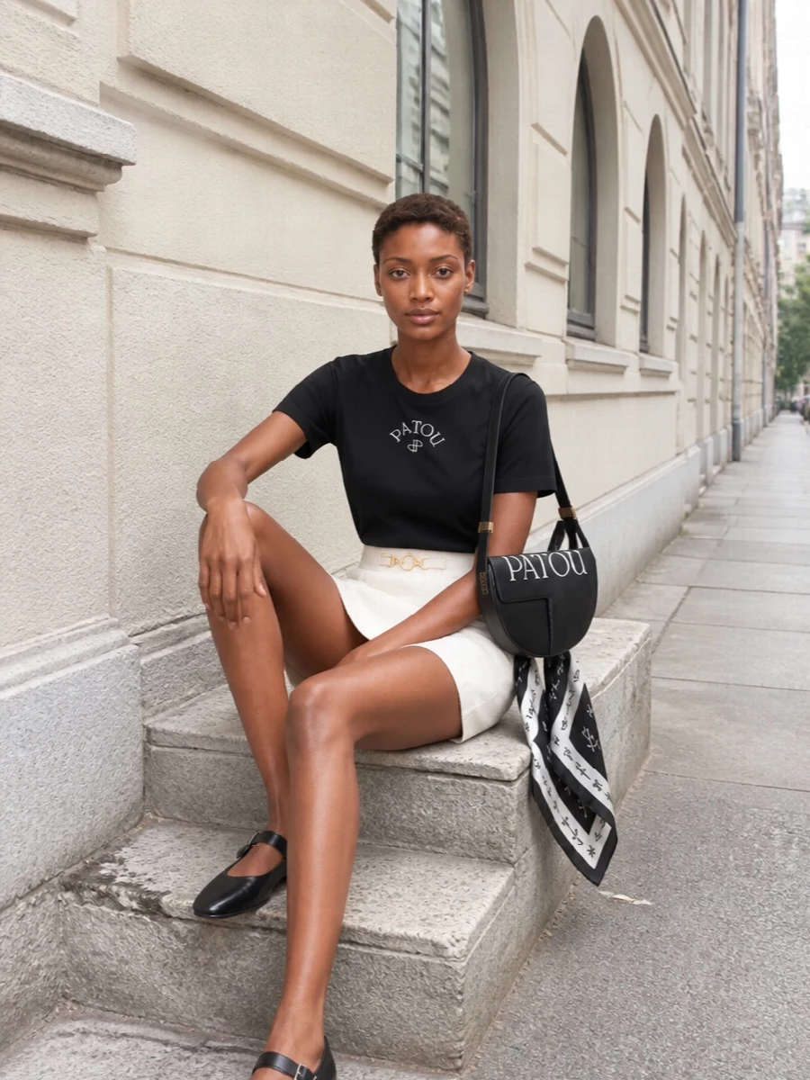 A black logo tee and ivory A-line mini create a crisp, Parisian contrast that reads polished but easy for daytime. The Mary Jane flats keep it grounded and preppy, while the structured half-moon bag and graphic silk scarf add just enough detail to feel intentional without losing the clean lines.