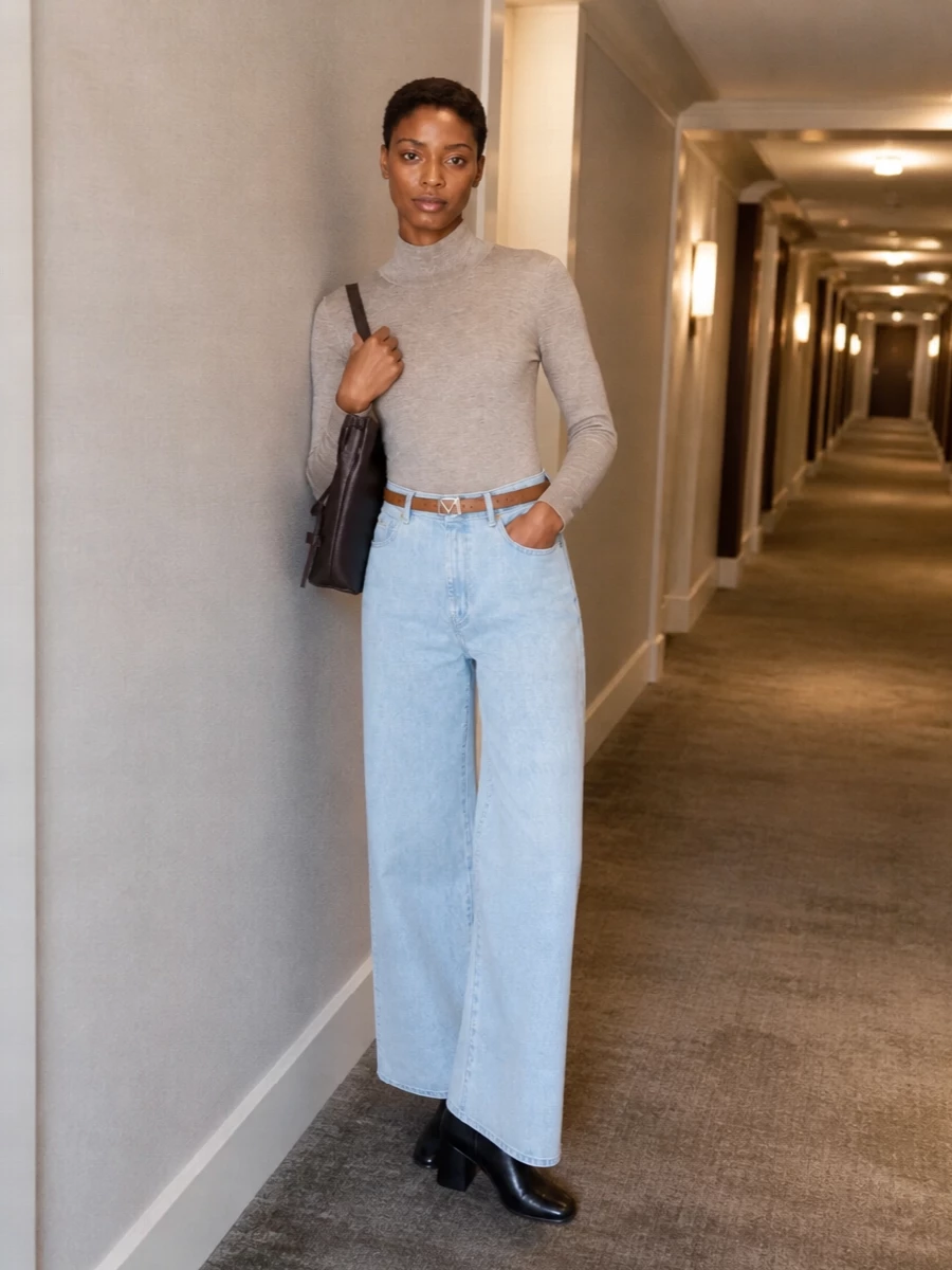 Soft neutrals meet pale architectural denim, with a slim mock-neck knit cleanly tucked to let the high-rise wide leg carry the silhouette. A tan belt and dark chocolate bucket bag quietly sharpen the waist and add depth, while black block-heel ankle boots ground the palette for city days that move into dinner. The result is relaxed, minimal and quietly precise, with the jeans as the central statement.