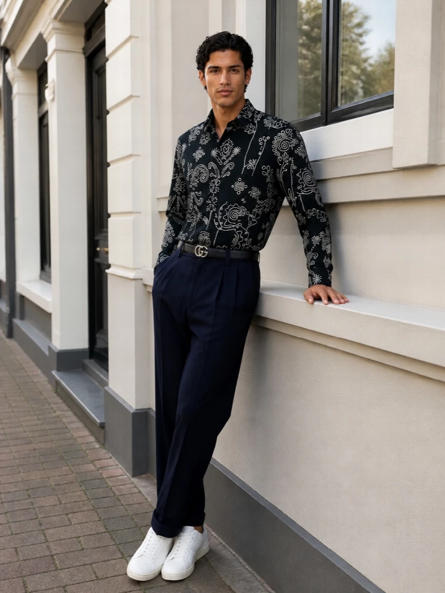 An inky floral shirt sits over relaxed pleated navy trousers, keeping the line fluid yet precise for gallery days and creative dinners. Off-white sneakers pick up the soft white in the print, while a navy monogram tote and ink belt ground everything in quiet, tailored polish. The result is romantic, modern and city-ready without feeling fussy.
