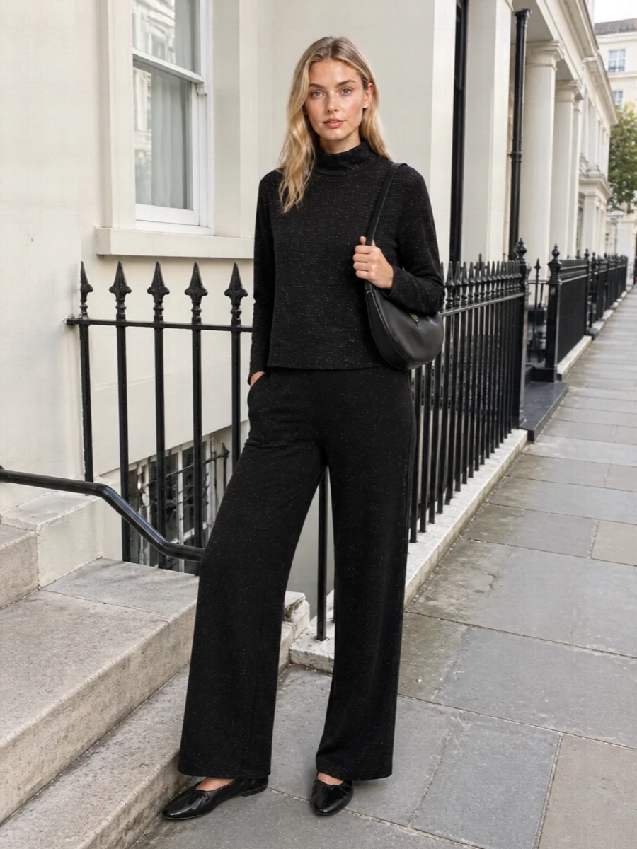 A black, subtly shimmering column sets a calm, refined mood, the wide leg balancing the mock-neck knit with relaxed movement. Soft glove-like flats keep the silhouette grounded and quiet, while the sculpted black shoulder bag adds just enough shine to echo the metallic thread without tipping into drama. It is an easy, polished option for low-key evenings when you want comfort that still feels considered.