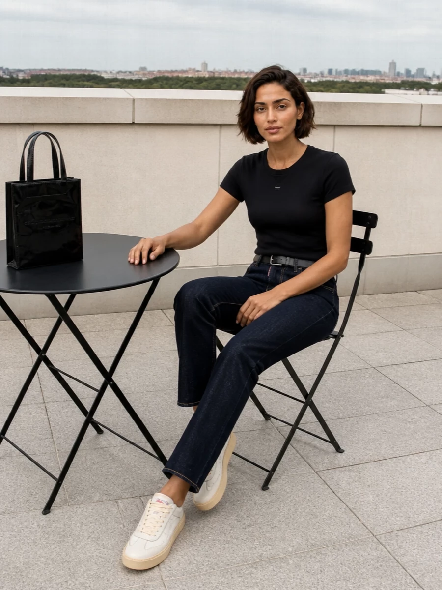 A black slim tee and dark indigo straight-leg denim create a clean, close-to-body line that feels modern and unfussy. Vintage-leaning off-white sneakers soften the monochrome without breaking the minimal mood. A glossy black mini tote and a razor-thin belt keep everything sharp and intentional while staying low key for all-day city wear.