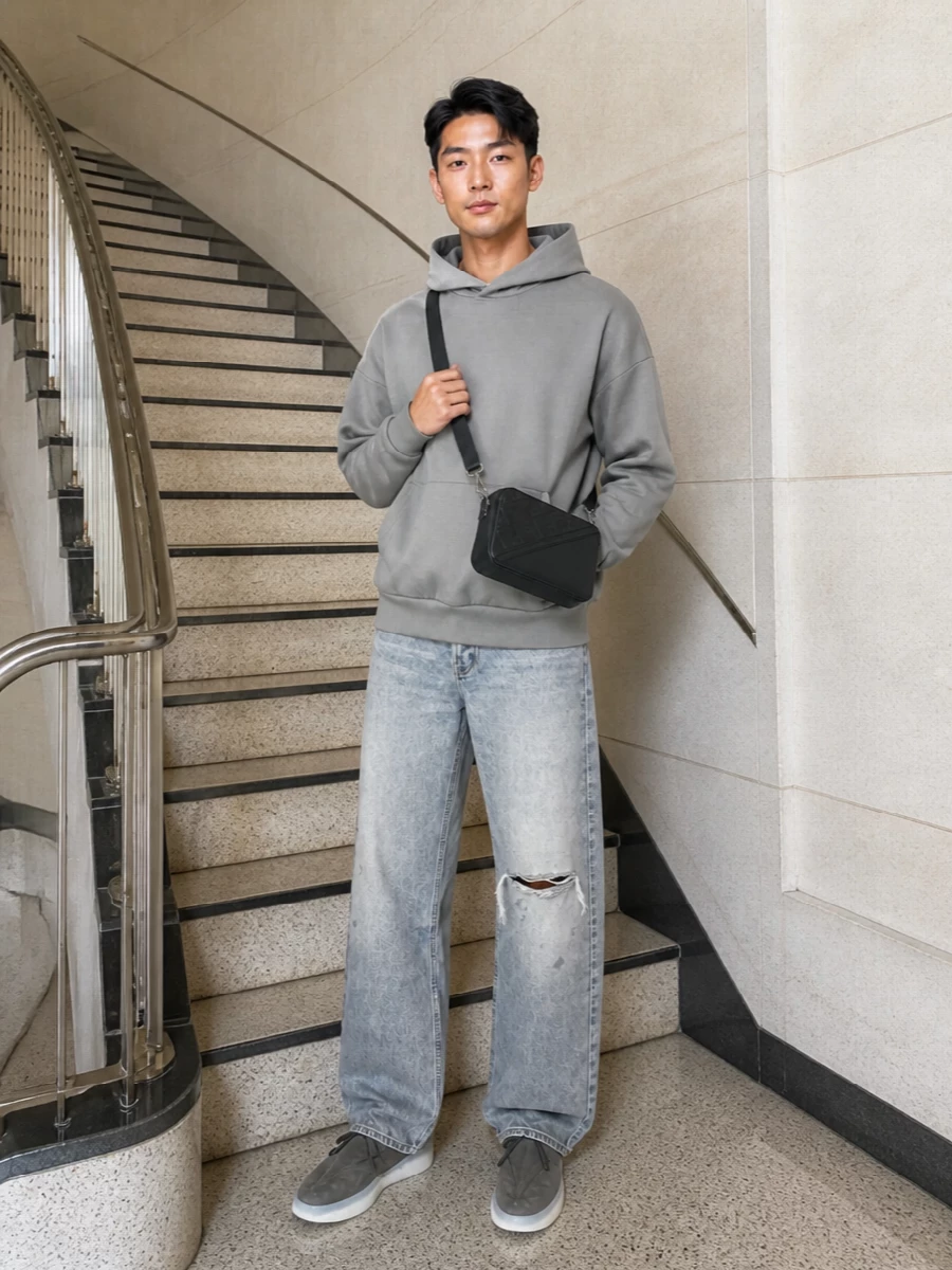 Washed grey denim and a stone hoodie sit in the same soft register, so the silhouette feels relaxed but intentional rather than thrown together. Sculpted runners and a structured crossbody pull in darker charcoals, giving the palette definition while keeping the attitude low-key and modern. It is an easy uniform for city days when you want grunge-leaning denim that still reads precise and considered.