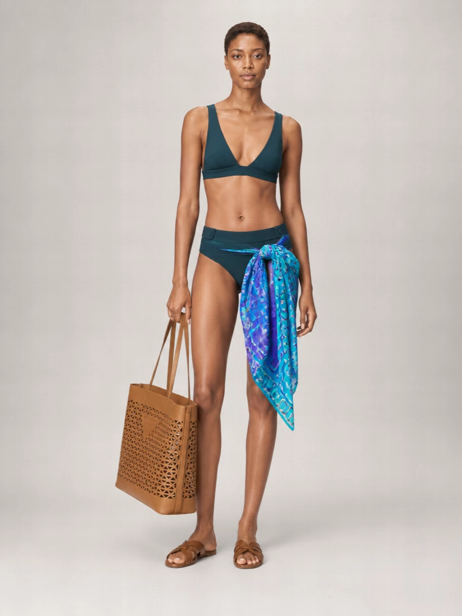 Deep teal Eres swimwear anchors this edit with clean lines and a quiet, sculpted V-neck that feels considered rather than bare. Tan leather slides and a structured Prada tote introduce soft warmth without cluttering the silhouette, while a Pucci pareo brings just enough print to suggest movement and personality around an otherwise minimal poolside uniform. The result is a calm, high-end beach ensemble that moves easily from lounger to lunch with everything reading precise and unfussy.