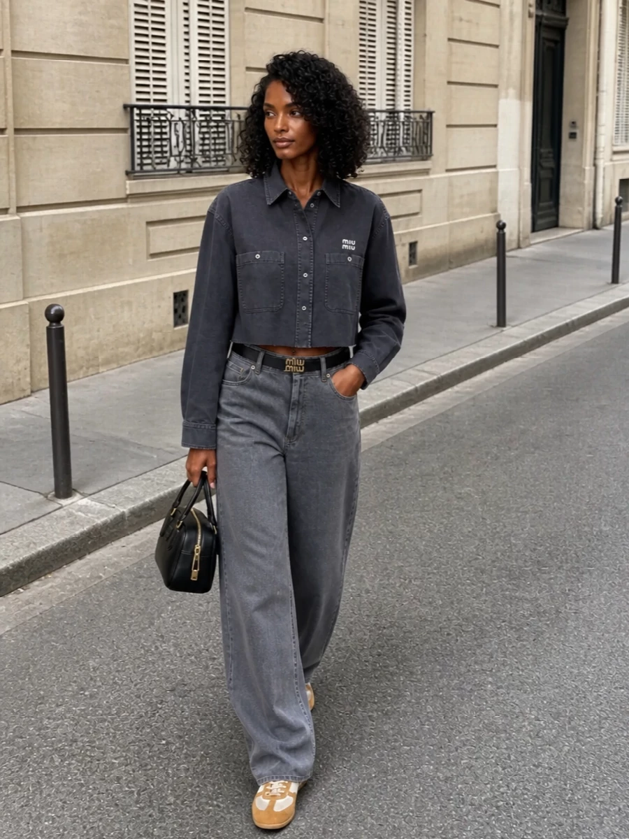 This look leans into a monochrome, quietly grunge-preppy mood: the cropped charcoal Miu Miu shirt sits sharp over slate-grey wide-leg denim for a long, relaxed line that still feels considered. Off-white and tan retro trainers keep it light and SS-ready, while a structured black mini bowler and slim logo belt sharpen the finish with just enough luxury hardware to signal Miu Miu without shouting.
