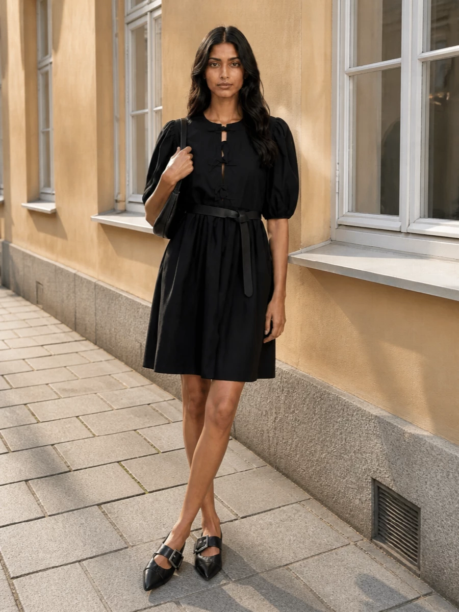A soft black A-line dress is grounded with pointed buckle flats and a sleek shoulder bag for a clean, feminine take on day dressing. The knot belt subtly defines the waist so the puff sleeves and bow detailing stay the quiet focal point. Wear it from coffee runs to low-key dinners without changing a thing.