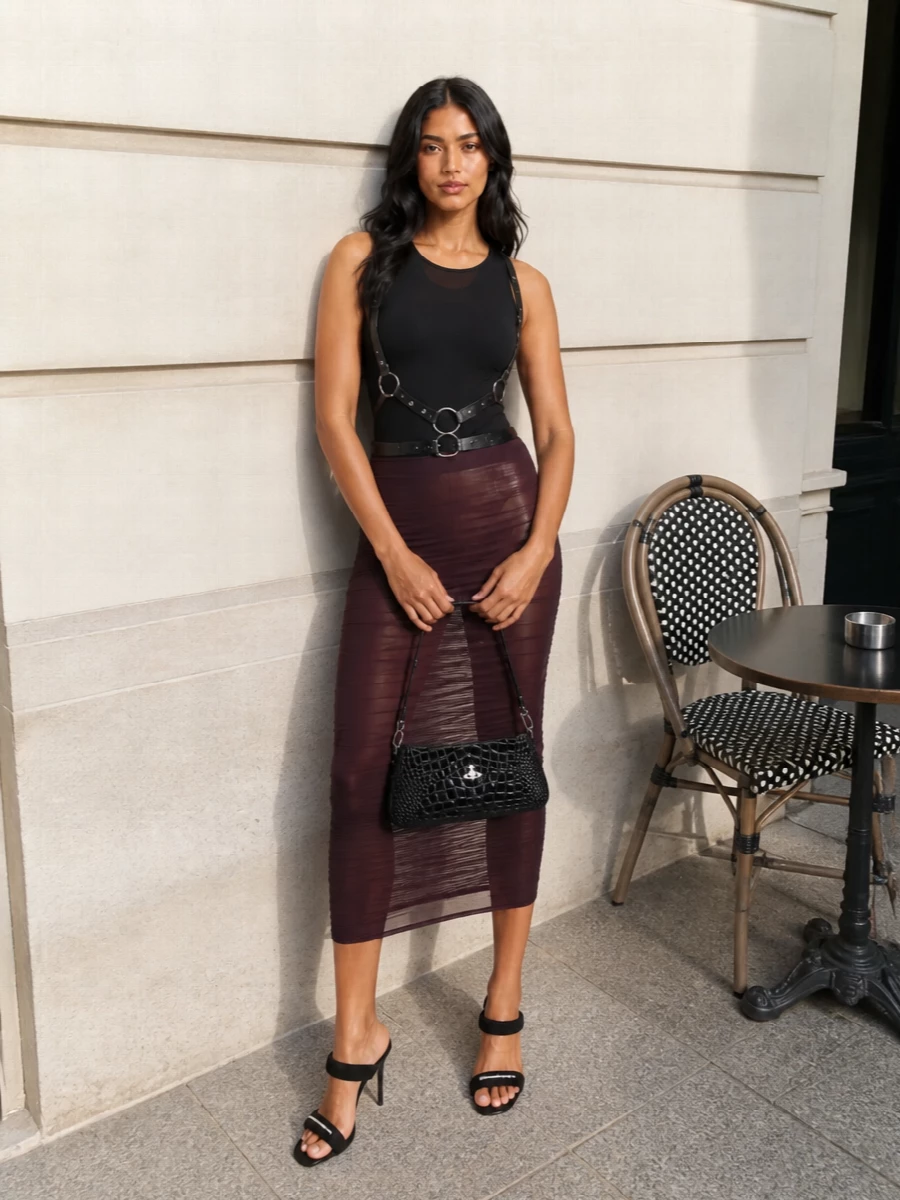 Deep plum mesh and a sculpting black bodysuit set a sleek, after-dark base that feels unapologetically body conscious. Stripped-back black mules keep the line clean and long, while a glossy croc baguette and harness hardware inject just enough subversive attitude. The result is a club-ready ensemble that reads polished, sharp and deliberately stacked in texture rather than color.