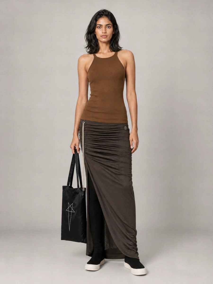 A long brown tank drops into a dark taupe ruched maxi, creating a fluid Rick-style column in tonal earth and shadow. Over-the-knee canvas sock boots sharpen the line and add height, while a flat black graphic tote keeps the mood urban and restrained. It is a quietly brutal, summer-weight take on grunge minimalism, ready for late days that roll into night.