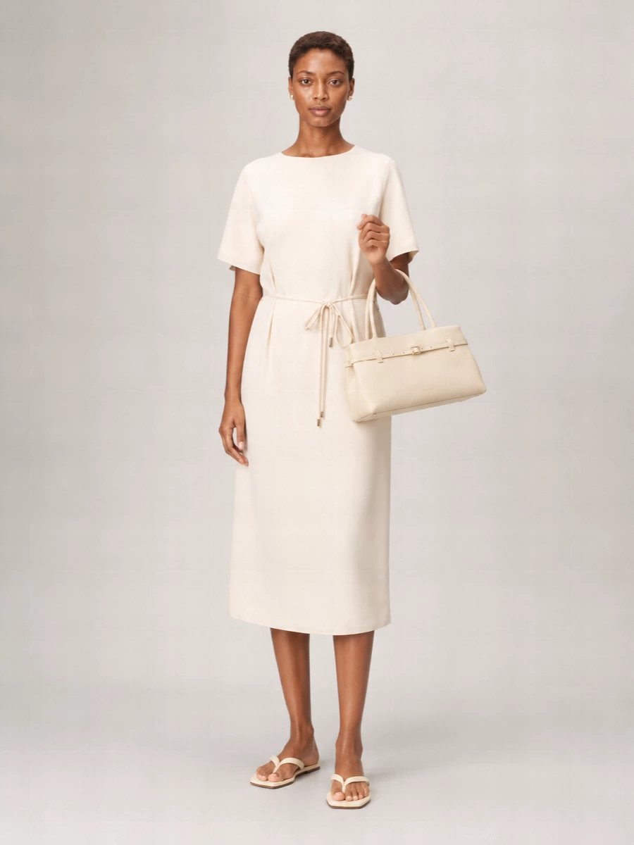 An ivory tonal story built around fluid lines and subtle definition, this outfit leans into quiet polish for warm city days. Barely-there cream sandals and a structured buttercream shoulder bag keep the mood light yet intentional, while a slim nude belt and small pearl studs add just enough detail without disturbing the dress’s clean softness. It is an easy desk-to-dinner ensemble that feels composed but never fussy.