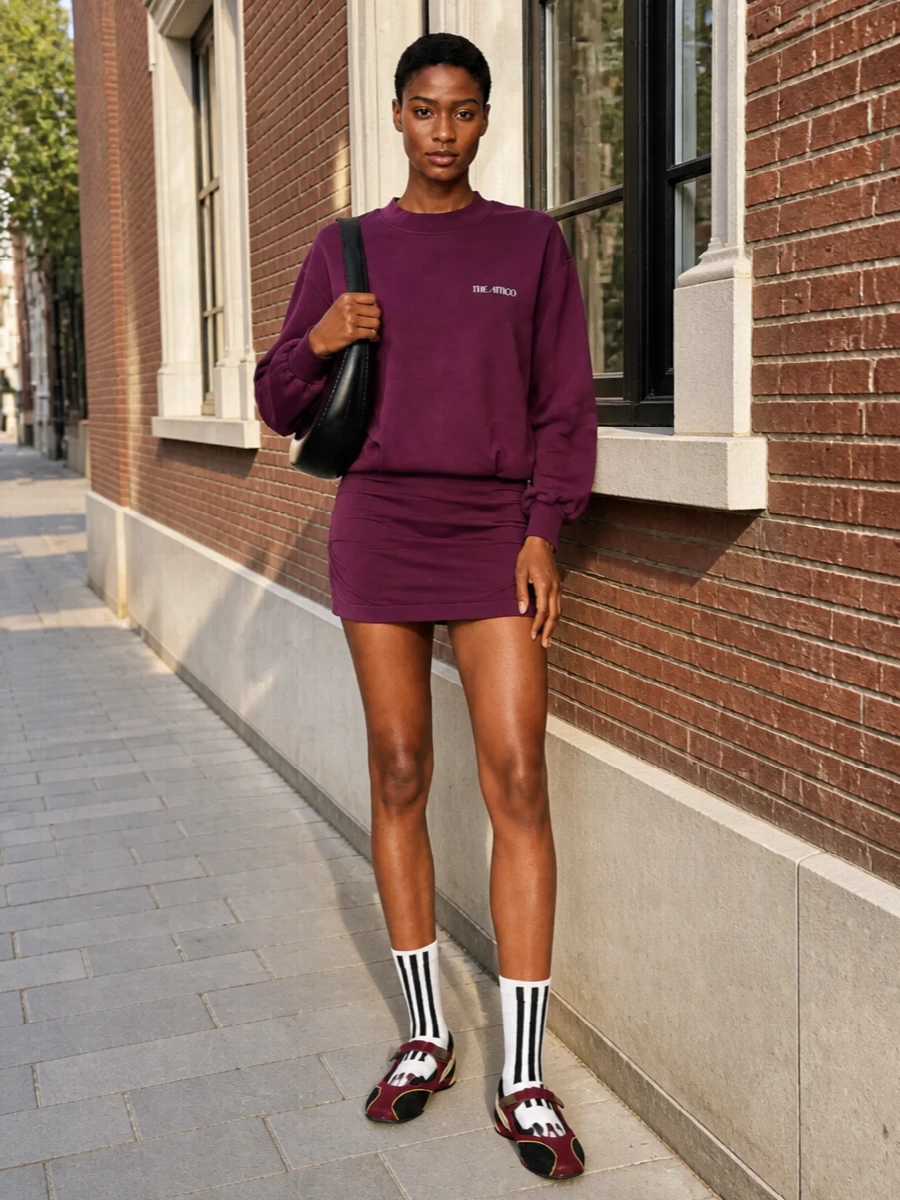 A plum Attico sweatshirt dress stays front and center, paired with burgundy technical Mary Janes for a sport-leaning, city-ready energy. White graphic socks keep the vibe casual, while a glossy black Coperni shoulder bag adds precise structure and polish. Wear it for travel days, coffee runs, or low-key dinners where you want comfort with clear intention.