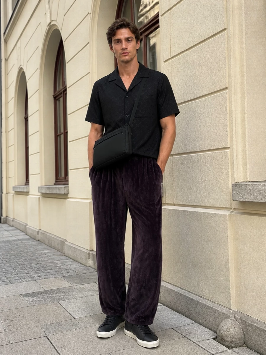 A boxy Gucci camp shirt sits over deep plum velvet wide-legs for a nocturnal mix of tailoring and street energy. Charcoal leather sneakers keep the line relaxed but intentional, while a padded black crossbody adds that insider, almost covert, detail-driven finish. It is a low-key, night-in-the-city uniform that feels rich in texture without ever shouting about it.