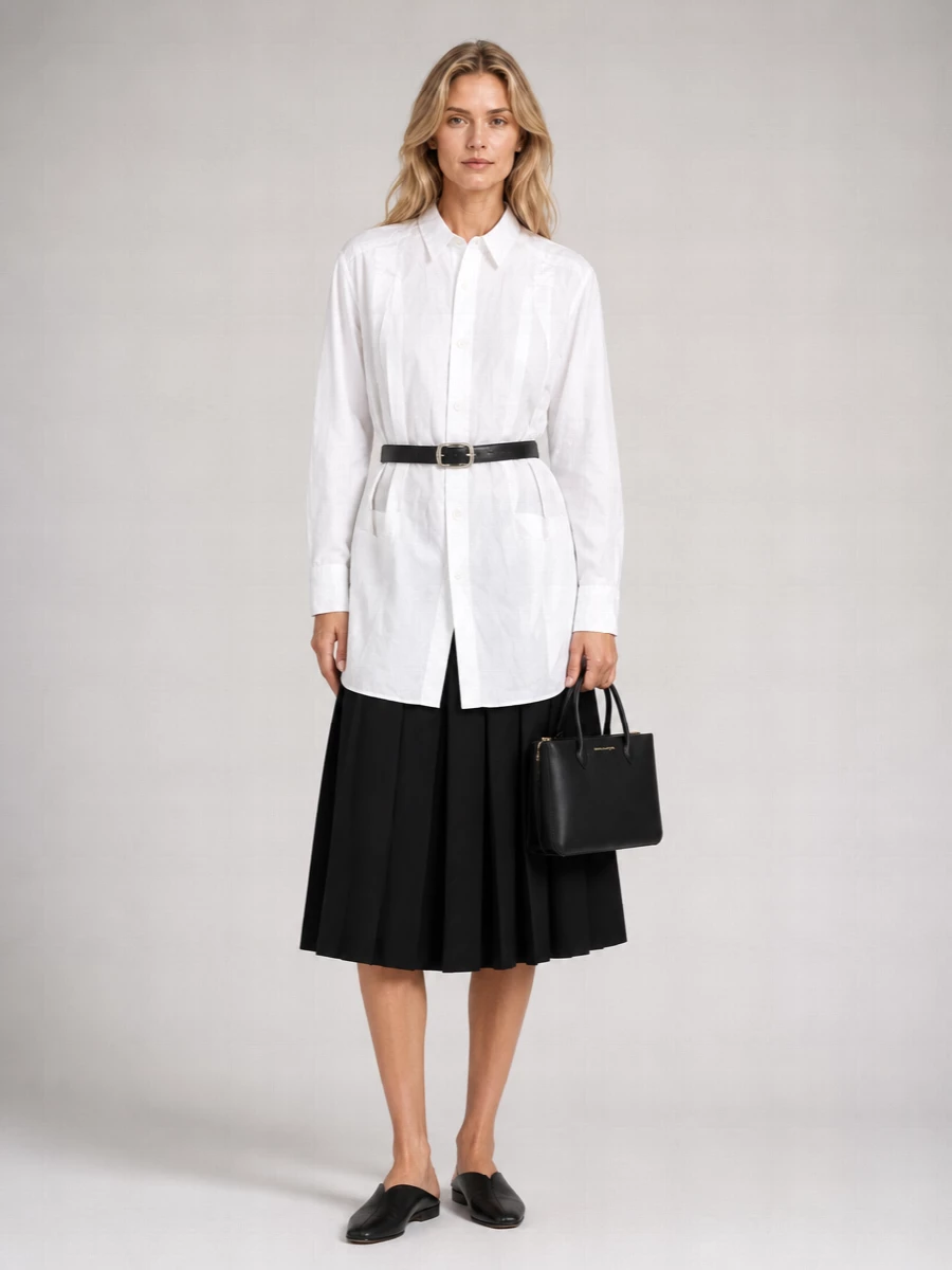 A monochrome study in structure, this pairing sets the crisp longline shirt against the inky pleated midi for a precise yet fluid silhouette. The square-toe flat and structured top-handle keep the mood quiet and assured, while a slim black belt lightly defines the waist without disturbing the clean architectural lines. It is polished enough for serious daytime settings, yet relaxed enough to carry into late gallery hours in the city.