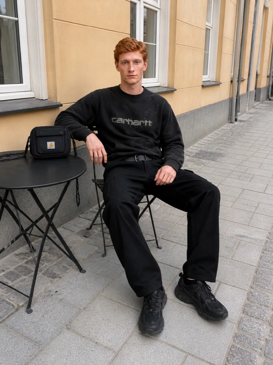 Black Carhartt cargos and the washed crew create a lived-in workwear base that feels graphic without loud logos. The all-black technical runners keep it agile and city-ready, while the compact crossbody and industrial belt add just enough structure to the loose, utility-heavy silhouette.