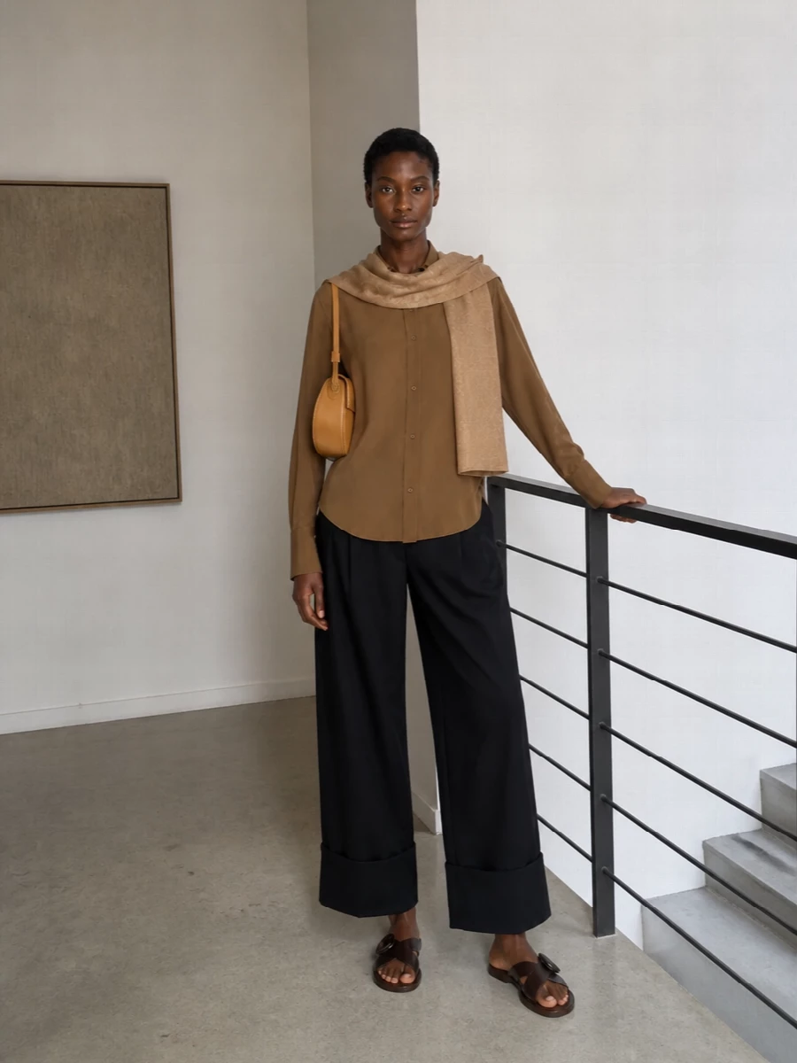 Camel and black are handled with precision here, letting the shirt’s scarf neckline and fluid drape take center stage against strong, cuffed tailoring. The wide black trouser and dark chocolate slingback create a long, graphic line, while the sculpted camel shoulder bag keeps the mood modern and discreet. It is a quietly powerful outfit that moves easily from serious daytime to intimate dinners without changing a piece.