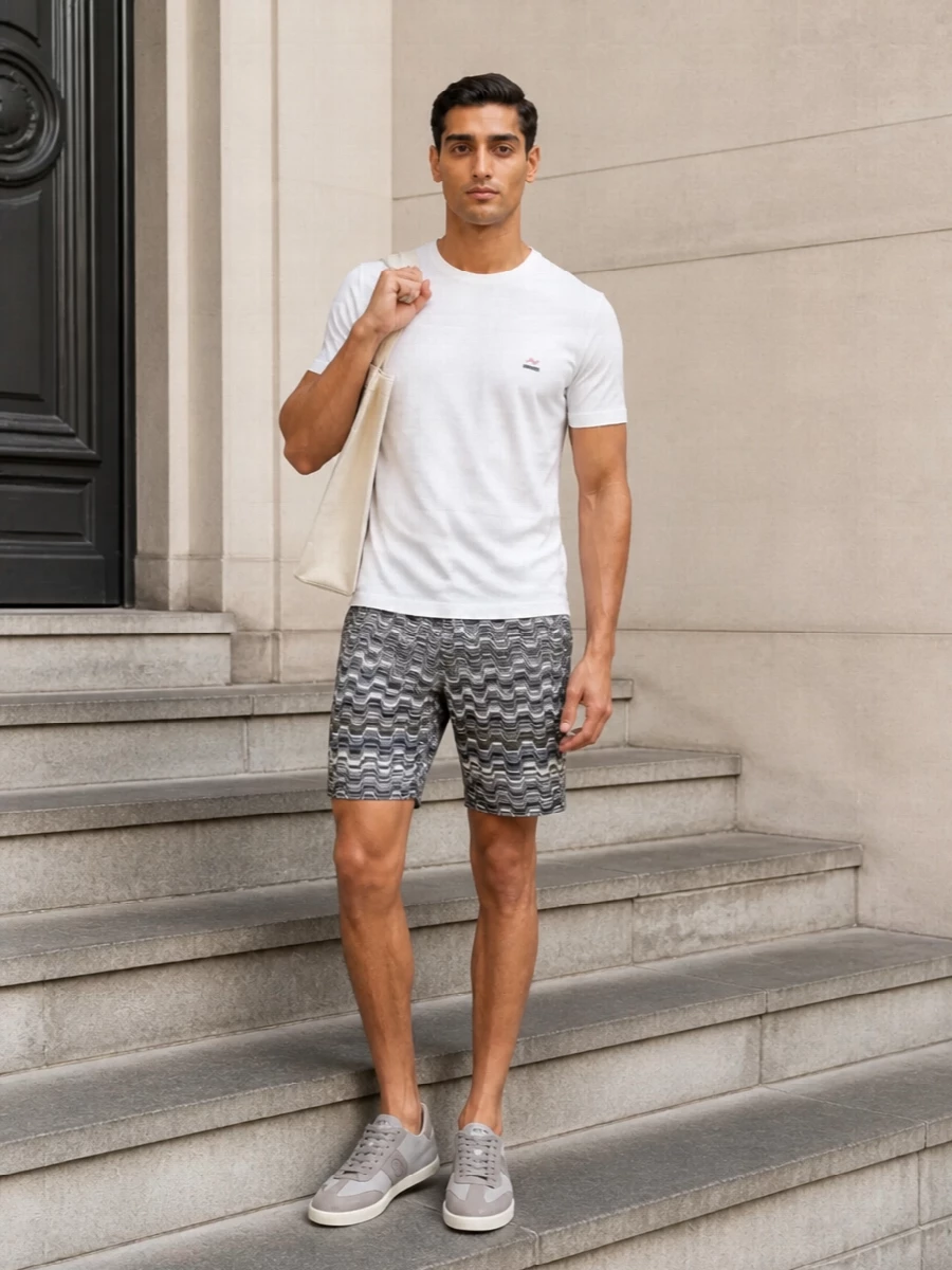 A crisp white Missoni tee pairs with tailored chevron shorts for a refined take on summer dressing that feels relaxed yet intentional. Soft grey and taupe sneakers keep the lines clean, while an off-white structured tote adds sculptural polish. The result is a quietly luxurious warm-weather outfit that works as naturally in the city as it does by the coast.