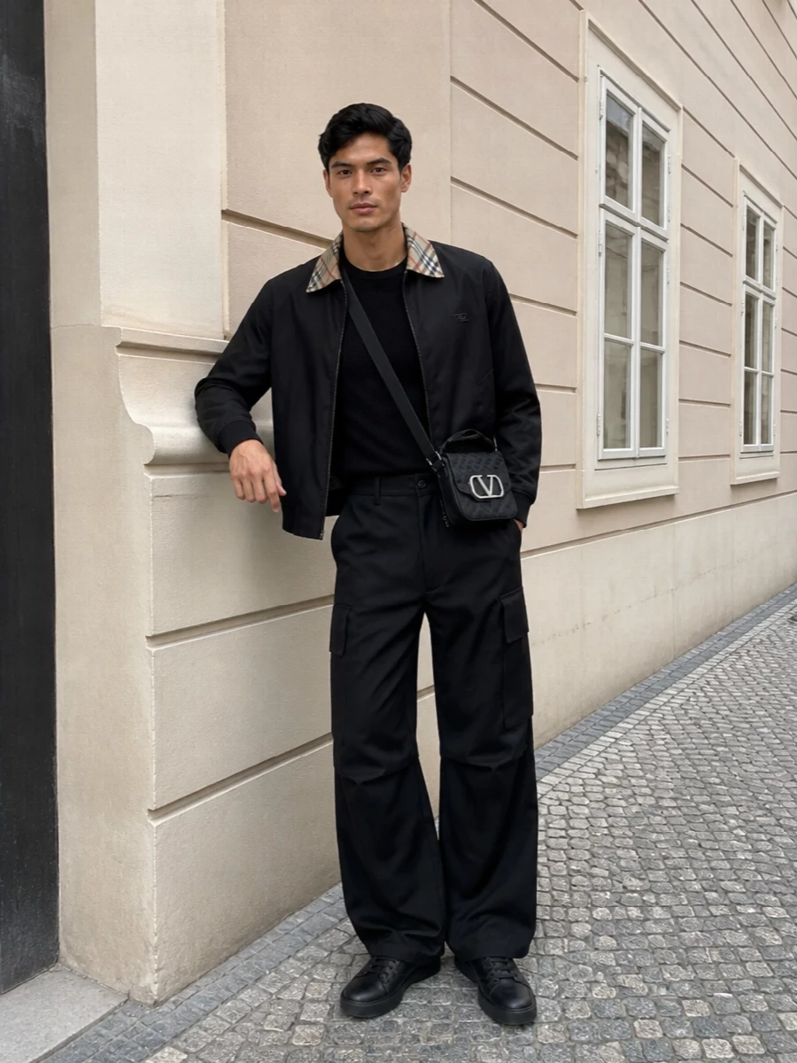Burberry’s clean bomber sits over a quietly detailed Moschino knit, grounding the heritage collar in a dark, modern base. Wide-leg Darkpark cargos and Balmain sneakers push the silhouette into confident streetwear territory while keeping everything monochrome and refined. A compact Valentino crossbody finishes it with a focused, city-ready edge that feels luxe but not loud.