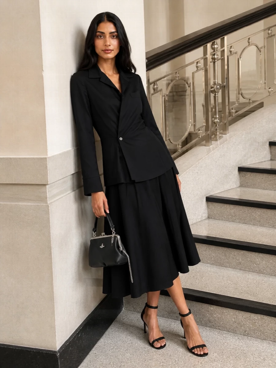 A sharply tailored black midi dress with an asymmetric wrap front channels a modern riff on evening suiting, perfectly in step with the structured Vivienne Westwood frame bag. Stripped-back black ankle-strap sandals keep the line long and graphic, letting the bag’s silver hardware read as the single, considered accent. Choosing the dress route over separates keeps the silhouette ultra-clean and formal, ideal for gallery openings or serious cocktail hours.