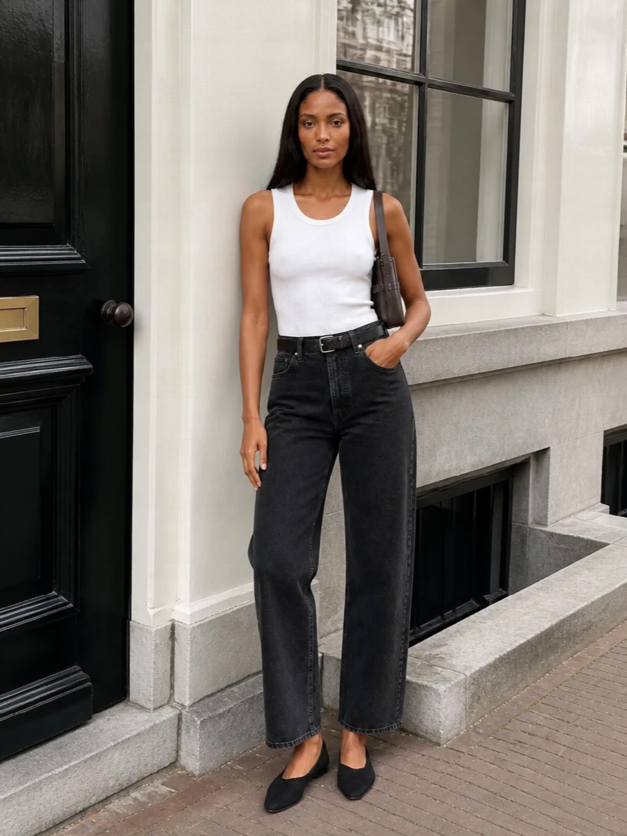 Washed black denim and a crisp white tank keep the outfit clean and intentional, all about line and proportion rather than fuss. A slim black belt and soft suede flats sharpen the silhouette without adding weight, while the chocolate shoulder bag introduces quiet warmth that still reads minimal and refined. It is an easy city uniform that feels considered from morning coffee to a low-key dinner.