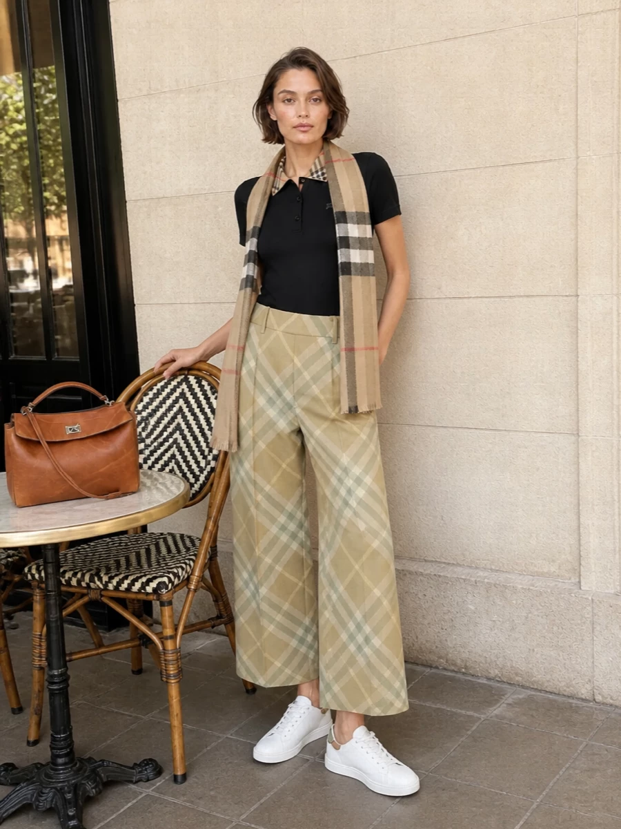 This look takes the sharp black Burberry polo and pairs it with high-rise cropped check trousers for a clean, tailored take on heritage preppy. Box-fresh white sneakers and a structured tan leather top-handle bag keep the mood modern and relaxed, while a light check scarf adds a final, refined Burberry echo that still feels fresh for spring-summer. The result is a quietly luxurious city uniform that moves effortlessly from daytime appointments to dinner.