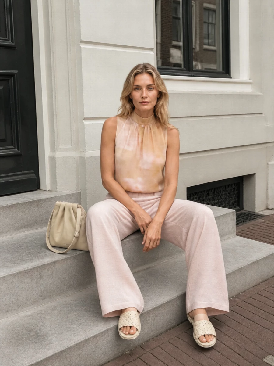A wash of blush, sand and cream creates a calm, elongated column that feels relaxed yet considered for warm days. The fluid scarf-top and wide-leg trouser move together, while low slides and a softly pleated hobo keep everything grounded and easy. Quiet texture and tone-on-tone color do the work so the outfit feels polished without ever looking overdone.