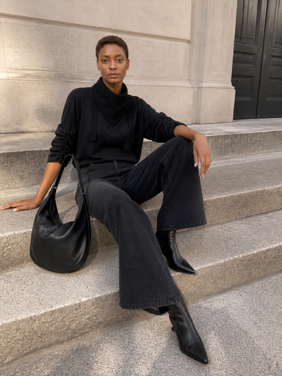 An all-Dries black base keeps the mood pared back yet directional, with the ruched sweatshirt and high-rise wide-leg trouser creating a long, sculpted line. Cone-heel ankle boots sharpen the proportions, while the oversized crescent bag and neat knit at the neck add quiet depth and practicality for city days. The result is relaxed, monochrome polish that still feels distinctly design driven.