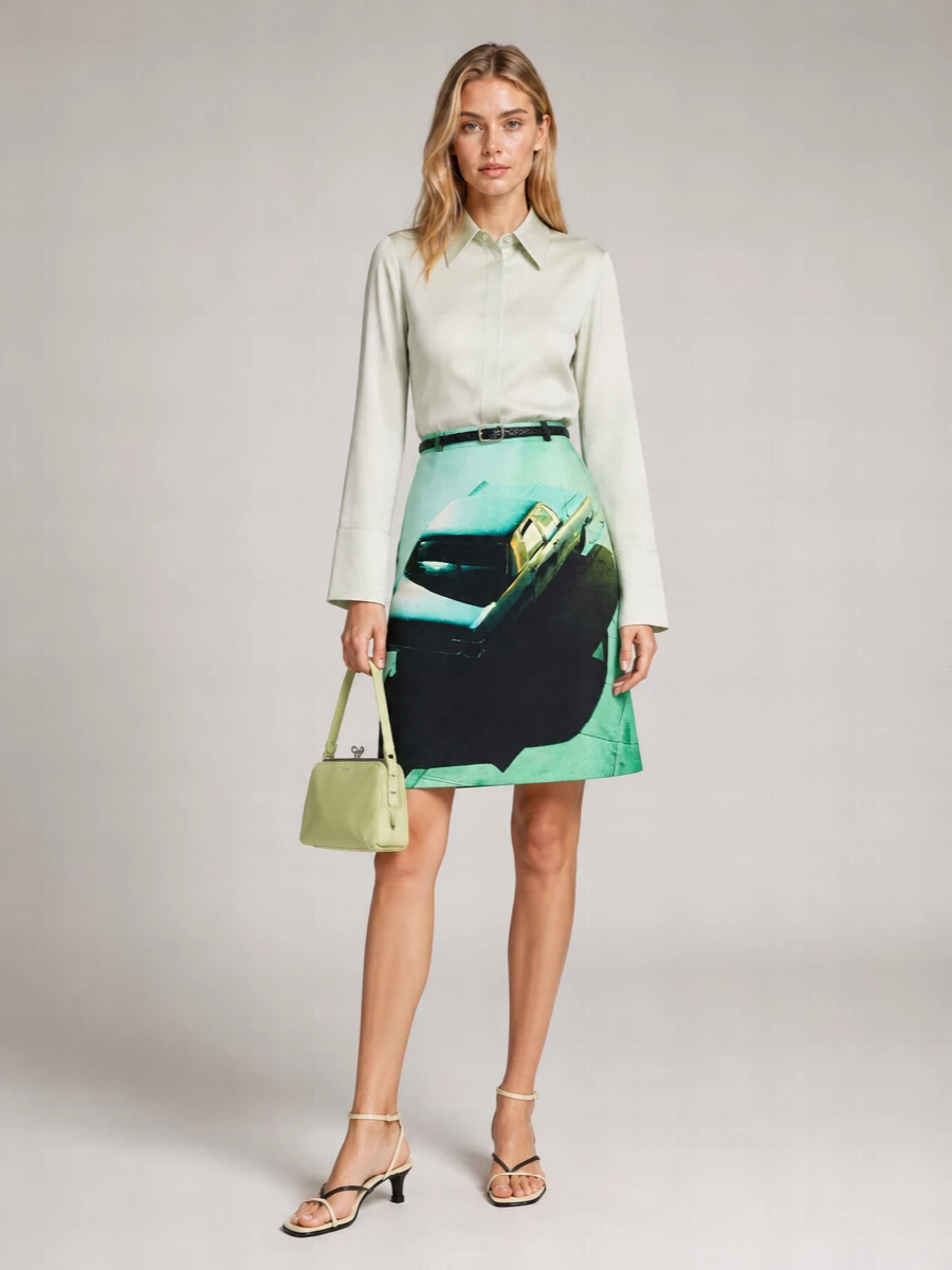 A cinematic mint-and-sage palette is kept calm with a fluid satin shirt and a sharply cut, high-waisted skirt, all grounded by black accents. Barely-there sandals and a pistachio frame bag keep the mood precise yet relaxed for city days that glide into dinner. The slim braided belt subtly defines the waist so the A-line volume feels intentional and sculpted rather than sweet.