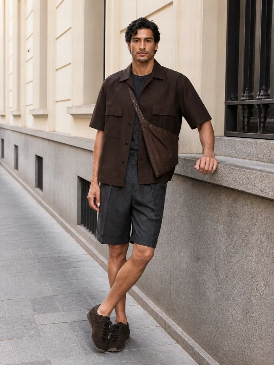 Sacai’s dark brown shirt jacket sits over a charcoal Stone Island base and pleated Jacquemus shorts, keeping the silhouette boxy up top and clean through the leg. Dark chocolate sneakers and a cocoa Kiko sling lock the palette into a rich, urban gradient that feels technical, grounded and quietly directional for warm city days and nights.