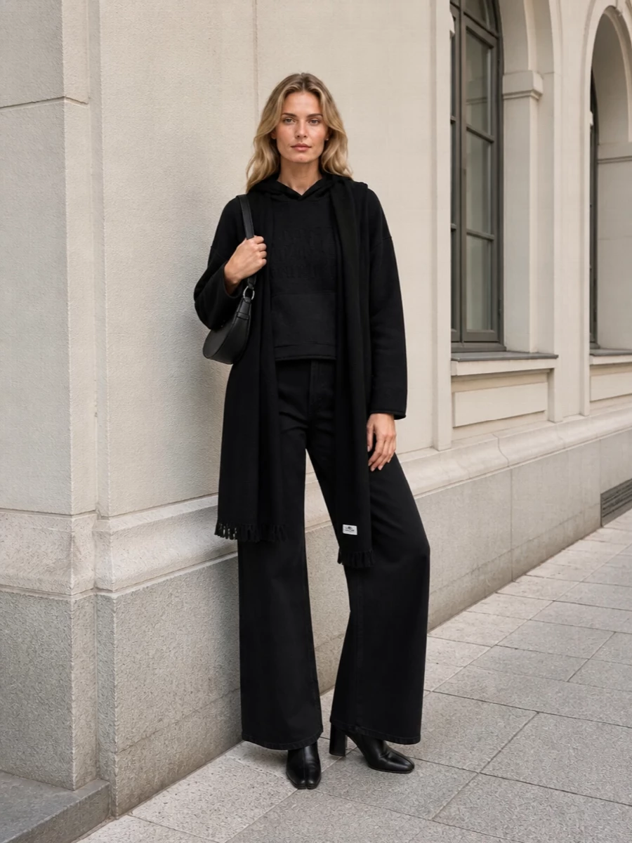Mm6’s black hoodie drops into a long, easy column of matching wide-leg trousers, keeping everything dark, graphic and quietly relaxed. Sleek Margiela ankle boots and a curved shoulder bag refine the line without disturbing the off-duty mood. A black scarf adds one last vertical stroke, so the whole outfit reads purposeful rather than casual.