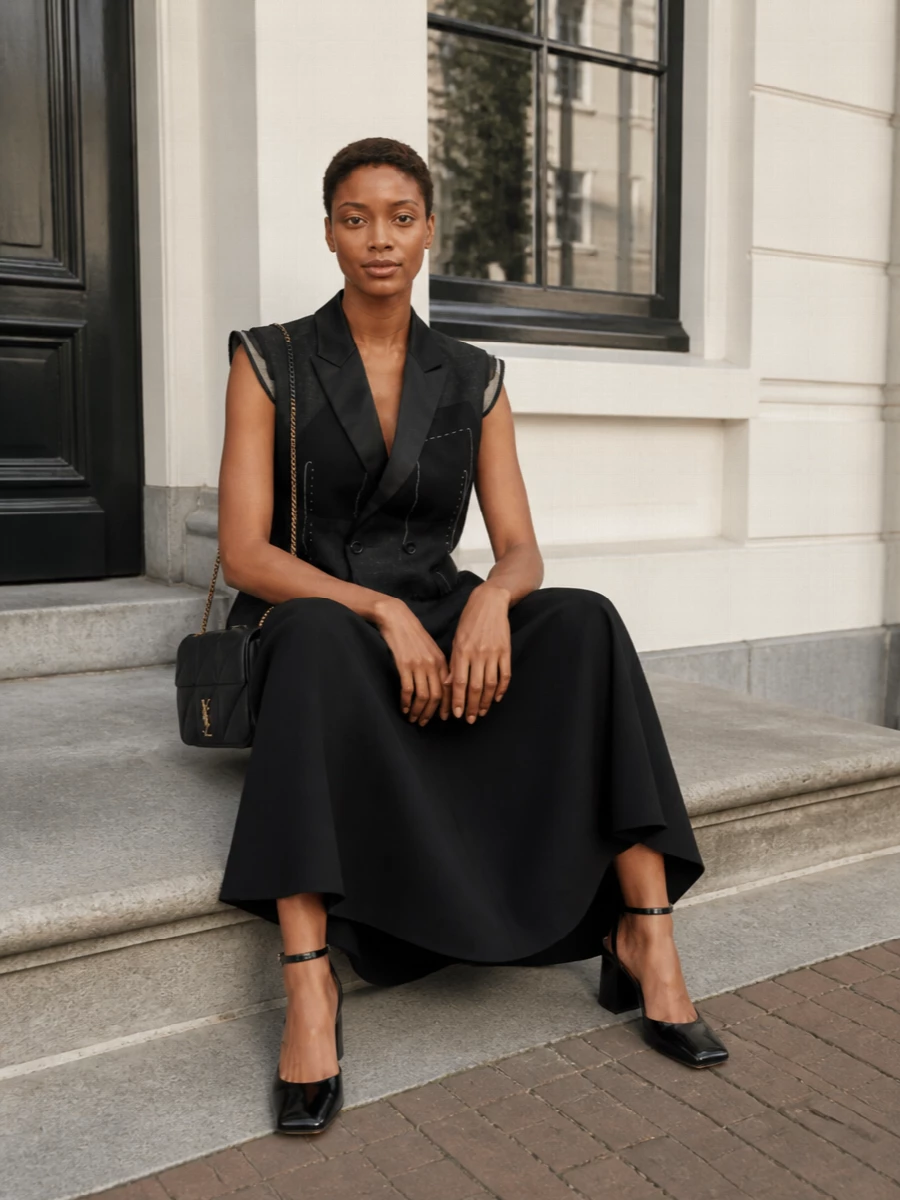 This pairing leans into a pure black-tie column, letting the tuxedo-cut Sacai dress and Saint Laurent shoulder bag carry a single, sharp line of evening polish. The Margiela sandals keep the focus on sculpted shape and texture rather than hardware, so the bag’s antique gold chain becomes the only glint. Choosing the dress route over separates preserves that uninterrupted, graphic silhouette that feels both modern and quietly luxurious.