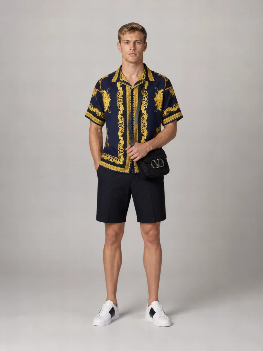 Versace’s baroque camp shirt sits over deep navy tailored shorts for a sharp, city-ready take on statement summer evenings. Clean white and navy sneakers and a compact black crossbody keep the drama contained to the print, reading confident rather than loud. It feels modern, luxurious and easy to wear from rooftop drinks to late-night bars.