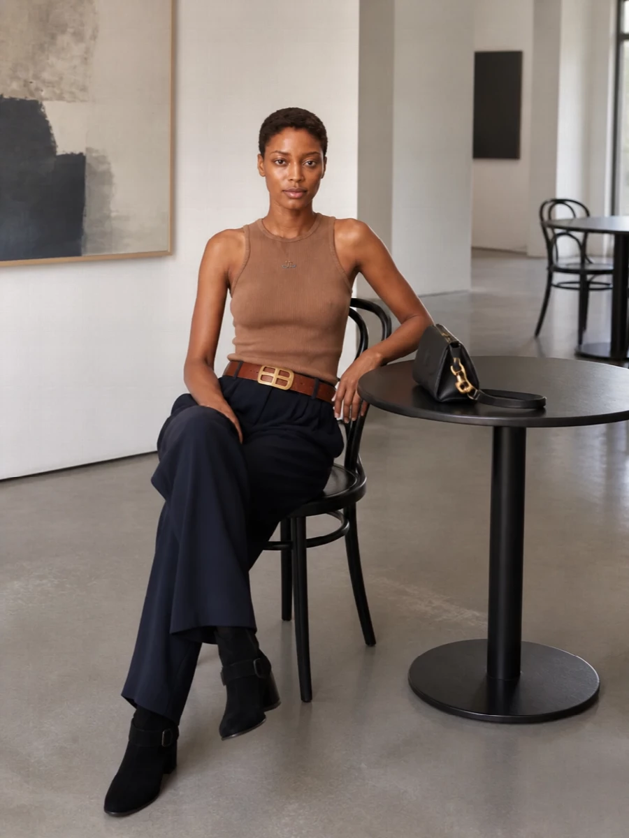 The camel ribbed tank is paired with deep navy wide-leg trousers for a clean, elongated line that feels calm yet intentional. Black block-heel ankle boots and a compact frame shoulder bag keep the palette grounded and refined, while a structured chestnut belt discreetly links the warm top to the deeper tones below. It is an easy, modern city uniform with quiet attitude rather than noise.