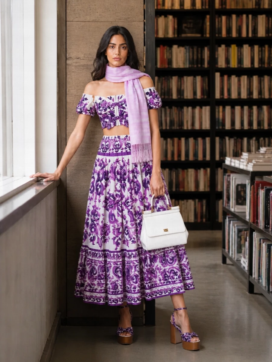 A romantic Dolce moment built around purple florals, this pairing of cropped off-the-shoulder top and tiered midi skirt creates a fluid, high-waisted column that feels lush yet relaxed. Violet platform sandals echo the print and keep the volume grounded, while a structured white top-handle bag and a whisper-soft pastel scarf bring just enough polish for garden parties, terraces, and destination dinners.