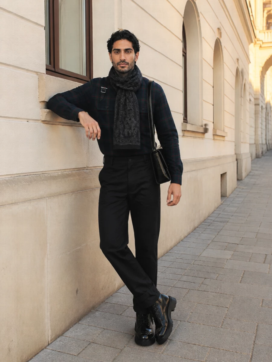 McQueen tartan meets uniform precision here, with utilitarian black trousers and assertive combat-style boots sharpening the shirt’s heritage pattern. The structured leather shoulder bag and skull scarf pull the palette into a tight, graphic city story, keeping everything street-leaning yet polished for colder days. Hardware details echo throughout so the outfit reads considered from collar to cuff.