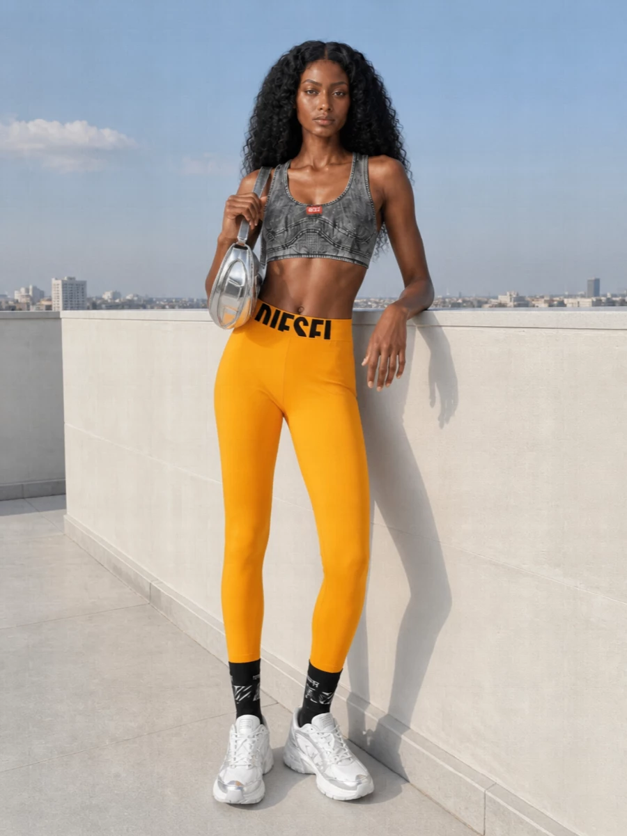 High-impact yellow Diesel leggings meet a dark, textured racerback crop for a tight, sport-heavy street set that feels ready for all-day movement. Chunky white and silver sneakers keep it grounded and practical, while the mirror-finish bag adds a sharp metallic hit that leans into the Y2K attitude. The logo socks are a small but deliberate styling touch, echoing the branding without stealing focus from the saturated base.